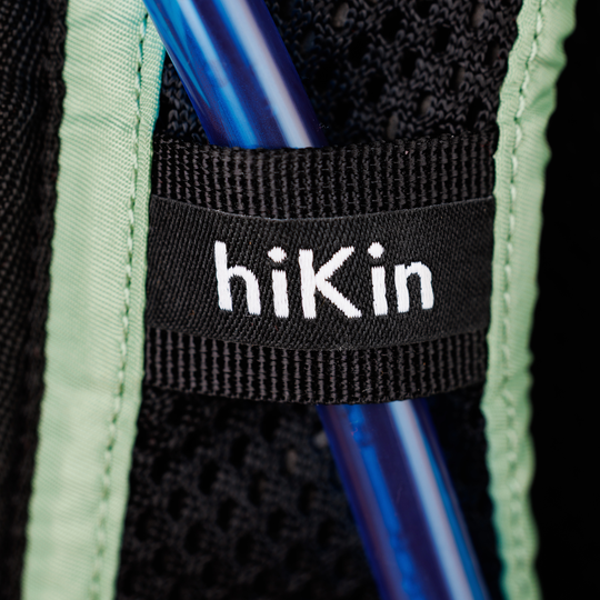 Close-up of a black backpack strap with the brand name 'hiKin' in white text, surrounded by mint green mesh fabric and a blue plastic tube.